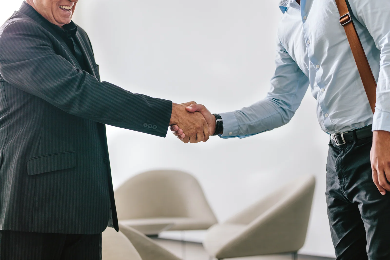 Two business men shaking hands in office. Senior businessman greeting and welcoming a young executive in office lobby.