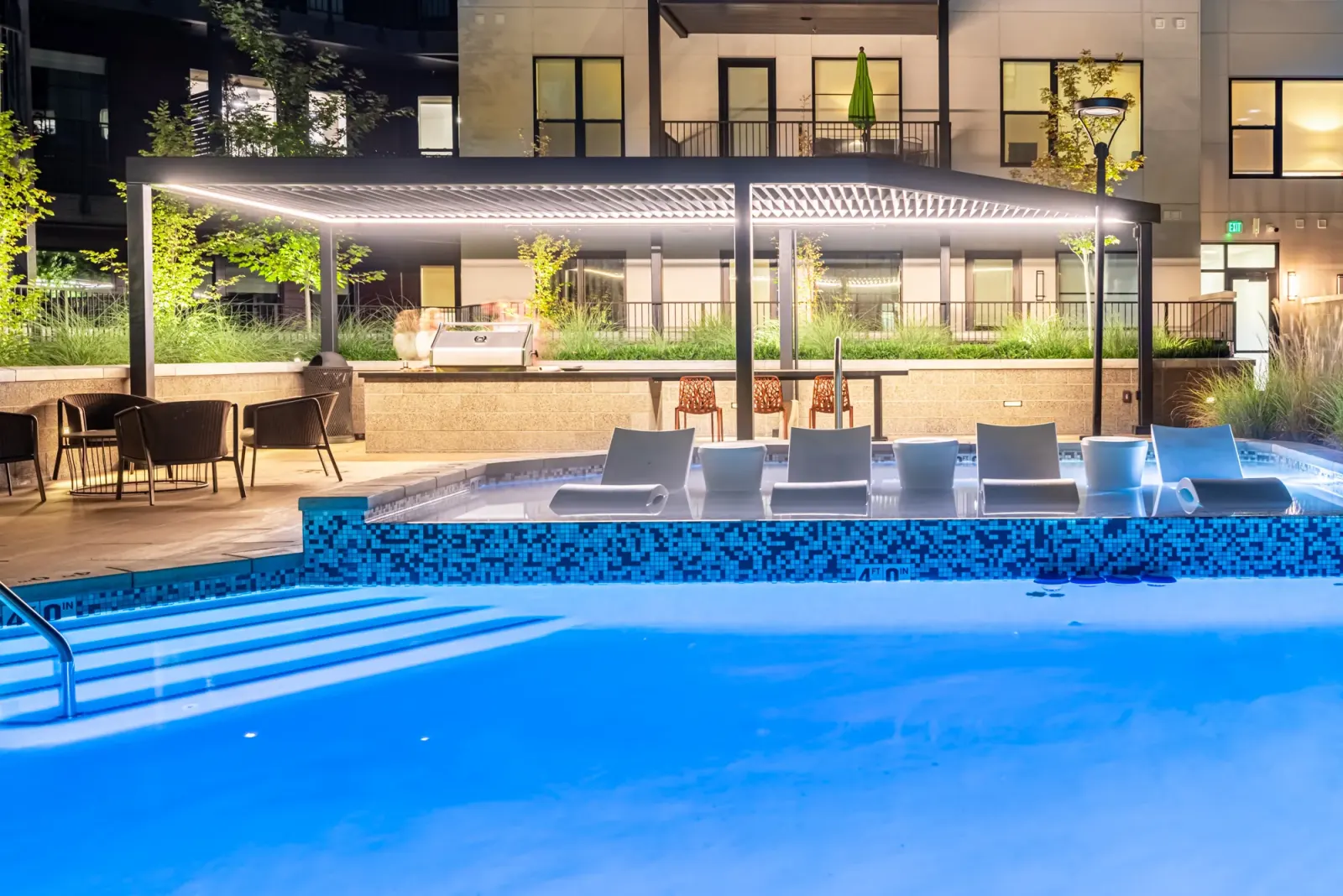 The Grandeur resort-style pool deck at dusk with tanning shelf and chevron pavilion.